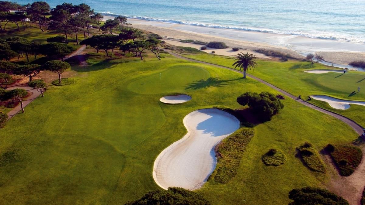 Aerial view of championship golf course meeting the Atlantic Ocean beach in the Algarve, Portugal — pristine fairways, sand bunkers and Mediterranean pines along the coastline