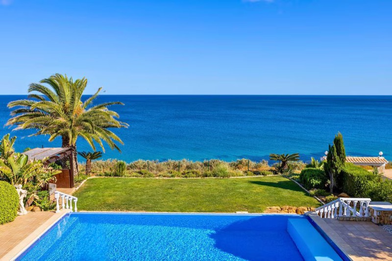 Private clifftop infinity pool framed by palm trees with a panoramic Atlantic Ocean view in the Algarve, Portugal